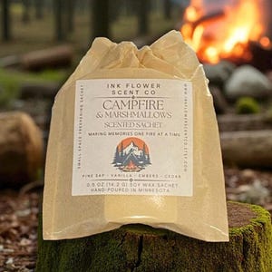 May include: A scented sachet in a clear, crinkled package, labeled "Campfire & Marshmallows" with a mountain and campfire graphic. The sachet contains 0.5 oz (14.2 g) of soy wax and is hand-poured in Minnesota. The background shows a campfire.