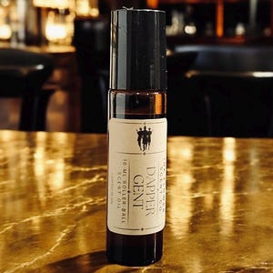 May include: A brown glass rollerball bottle with a black cap. The bottle is labeled "Dapper Gent" and "10 ml Roller-Ball Scent Oil".