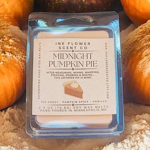 May include: A blue and white wax melt container with the text "Ink Flower Scent Co. Midnight Pumpkin Pie" and a description of the scent notes: "Pie Crust - Pumpkin Spice - Vanilla". The container is surrounded by pumpkins.