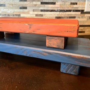 Puede incluir: Dos soportes de madera en niveles, uno pintado de naranja desgastado y el otro de azul desgastado. Los soportes están apilados uno encima del otro.