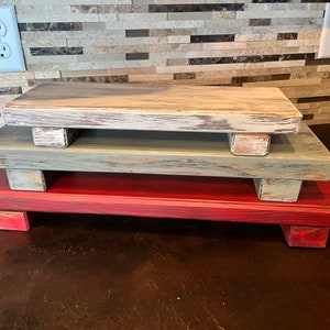 May include: Three tiered wooden trays in red, green and white distressed paint. The trays are stacked on top of each other and have a rustic farmhouse style.