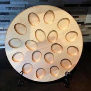 Puede incluir: Una bandeja redonda de madera para servir con 20 hendiduras individuales para contener huevos. La bandeja está hecha de madera clara y tiene un acabado natural.