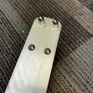 May include: A silver metal bar with four silver metal screws. The screws have round heads.