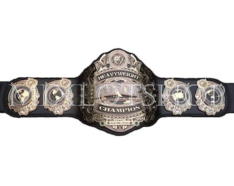 Pode incluir: Um cinturão de campeonato com uma correia de couro preta e detalhes em metal dourado. A placa central diz "Heavyweight Champion" e apresenta um emblema de leão. As placas laterais exibem desenhos de mapas mundiais.