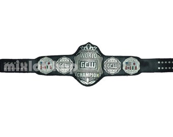 May include: A black leather wrestling championship belt with silver metal detailing. The central plate reads "WORLD GCW CHAMPION" and features a crown. Side plates display "GCW" and flags. The belt has adjustment holes.