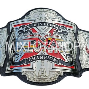 May include: A wrestling championship belt with a black leather strap and a large, ornate silver and red metal plate. The plate features the text "X-DIVISION" and "TNA WRESTLING CHAMPION".