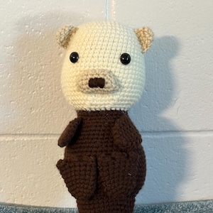 May include: A crocheted stuffed otter toy with a white head and brown body. The otter has black eyes and a brown nose.