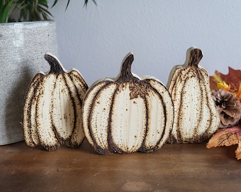 May include: Three wooden pumpkins with a burnt wood design. The pumpkins are light brown and have a natural wood grain.