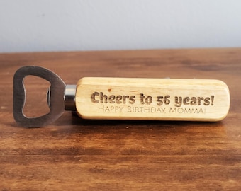 May include: A wooden bottle opener with a metal opener and a handle that says "Cheers to 56 years! Happy Birthday Momma!"