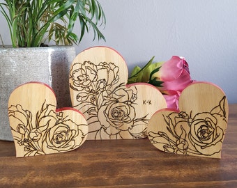 May include: Three wooden heart-shaped ornaments with a laser-etched design of roses and leaves. The largest heart has the initials "K+K" etched on it.