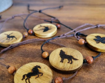 May include: Five wooden bracelets with different animal silhouettes burned into the wood. Each bracelet has a brown cord and brown wooden beads.