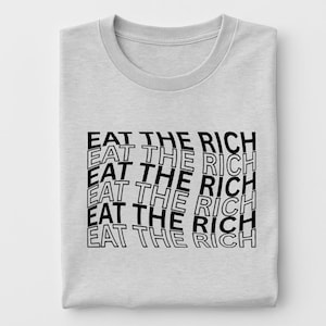 Peut inclure: Un t-shirt gris clair à col rond avec l'inscription "EAT THE RICH" en noir, superposée et ondulée sur le devant. Le texte est en gras, en police sans-serif.