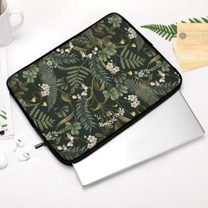May include: A dark green laptop sleeve with a floral pattern featuring white flowers and green leaves. The sleeve is made of a soft, durable material and is designed to protect your laptop from scratches and bumps.