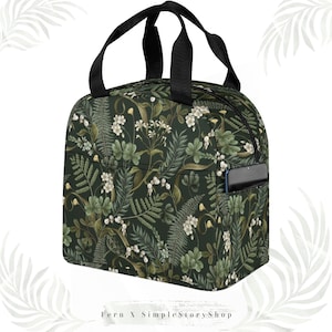 May include: A dark green insulated lunch bag with a floral pattern featuring white flowers and green foliage. The bag has a black zipper, black handles, and a pocket with a phone inside. The text "Fern X SimpleStoryShop" is at the bottom.