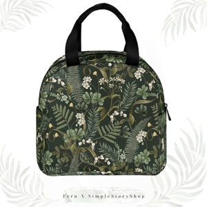May include: A round, insulated lunch bag with a black handle and zipper. The bag features a dark green floral pattern with white flowers and green leaves. The text "Fern X SimpleStoryShop" is at the bottom.