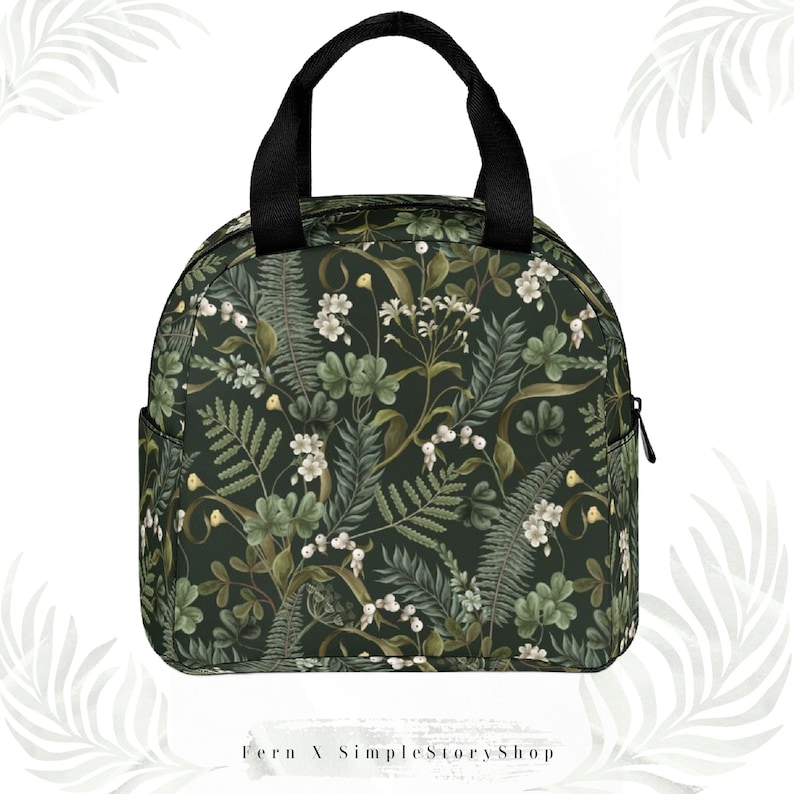 May include: A round, insulated lunch bag with a black handle and zipper. The bag features a dark green floral pattern with white flowers and green leaves. The text "Fern X SimpleStoryShop" is at the bottom.