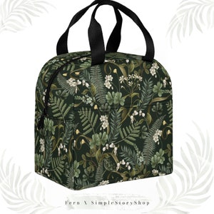 May include: A dark green insulated lunch bag with a botanical pattern of white flowers, ferns, and other foliage. The bag has a black zipper, black handles, and the text "Fern X SimpleStoryShop" at the bottom.
