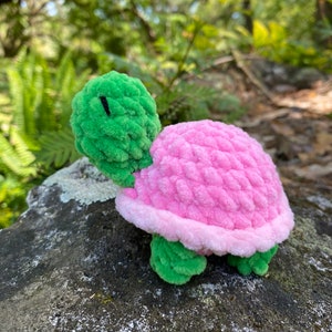 Pode incluir: Um pequeno brinquedo de tartaruga de croch&ecirc; com cabe&ccedil;a verde e concha rosa.