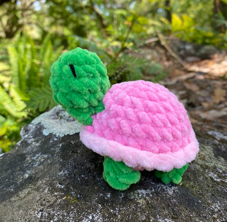 Pode incluir: Um pequeno brinquedo de tartaruga de croch&ecirc; com cabe&ccedil;a verde e concha rosa.