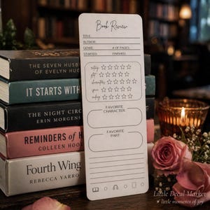 May include: A white bookmark with the words "Book Review" at the top. It has sections for title, author, genre, and rating. The bookmark is next to a stack of books with titles like "The Seven Husbands of Evelyn Hugo."