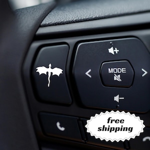 May include: Black car steering wheel buttons with white symbols. One button features a white dragon silhouette. Other buttons control volume, mode, and phone functions. The image also includes a "free shipping" sticker.