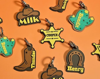 Può includere: Una collezione di portachiavi a tema western con vari disegni, tra cui un ferro di cavallo, un cappello da cowboy, un cactus, un distintivo da sceriffo e uno stivale da cowboy. Ogni portachiavi ha un anello argentato e un nome, come "Oliver", "Milk", "Rocky" e "Bandit".
