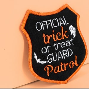 May include: Black felt patch with orange stitching in the shape of a shield. The patch says "OFFICIAL trick or treat GUARD Patrol" in white embroidery with a small ghost and bat graphic.