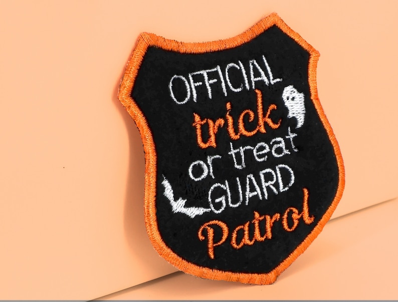 May include: Black felt patch with orange stitching in the shape of a shield. The patch says "OFFICIAL trick or treat GUARD Patrol" in white embroidery with a small ghost and bat graphic.