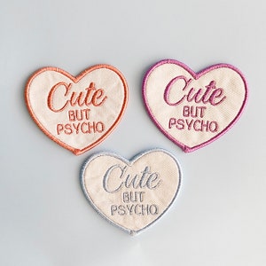 May include: Three heart-shaped patches with white fabric and embroidered pink, orange, and blue outlines. Each patch features the text "Cute but Psycho" in a cursive font.