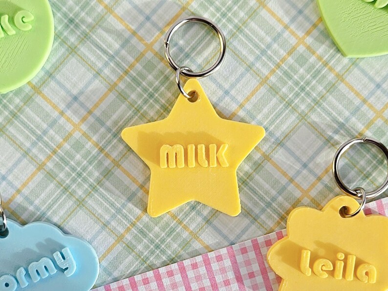 May include: A yellow star-shaped keychain with the word "milk" embossed in the center. The keychain features a silver metal split ring attached to the top point of the star, allowing for easy attachment to keys or other personal items.