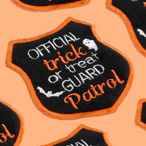 May include: Black felt patch with orange stitching shaped like a shield. It says "OFFICIAL trick or treat GUARD Patrol" in white embroidery with a ghost and bat graphic.
