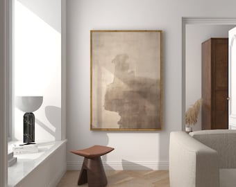 May include: A light brown abstract painting in a gold frame hangs on a white wall above a brown wooden stool. A white lamp sits on a windowsill in the background.