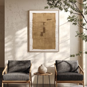 K&ouml;nnte beinhalten: Zwei dunkelgraue Sessel mit Holzrahmen, ein kleiner runder Tisch mit einem schwarzen Metallgestell und eine Keramikvase mit hellbrauner Glasur. Ein gerahmtes Kunstwerk mit einer braunen gewebten Textur h&auml;ngt an der Wand hinter den St&uuml;hlen.