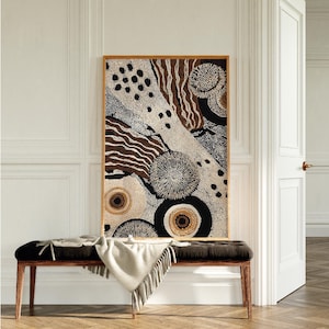 K&ouml;nnte beinhalten: Abstrakter Kunstdruck in einem Holzrahmen. Das Kunstwerk zeigt eine Mischung aus braunen, schwarzen und cremefarbenen Farben mit kreisf&ouml;rmigen und linearen Mustern. Der Druck wird &uuml;ber einer schwarzen Bank mit einer cremefarbenen Decke angezeigt.