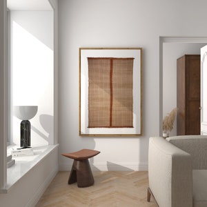 May include: A brown woven wall hanging with a red stripe in the center, framed in a light wood frame, hanging on a white wall in a living room setting.
