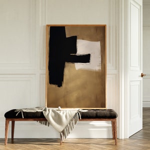 May include: Abstract art print with black and white brushstrokes on a gold background. The print is framed in a natural wood frame and is hanging on a white wall.