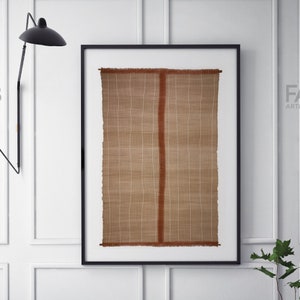 May include: A framed wall hanging with a woven texture in shades of brown and white. The woven piece has a vertical red stripe down the center.