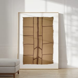 May include: A framed abstract wall tapestry with a brown and beige geometric design. The tapestry has a rough, textured surface and a frayed edge.