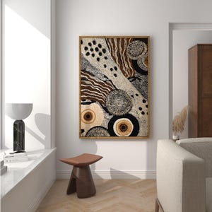 K&ouml;nnte beinhalten: Abstrakter Kunstdruck in einem Holzrahmen. Das Kunstwerk zeigt eine Mischung aus beige, braunen und schwarzen Mustern, darunter Punkte, Linien und kreisf&ouml;rmige Formen. Das St&uuml;ck wird in einem hellen Raum mit moderner &Auml;sthetik ausgestellt.