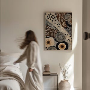 K&ouml;nnte beinhalten: Abstrakte Wandkunst mit einem beige-, braun- und schwarzen Muster. Das Kunstwerk weist kreisf&ouml;rmige und lineare Designs auf, die ein strukturiertes Aussehen erzeugen. Das gerahmte St&uuml;ck wird an einer wei&szlig;en Wand ausgestellt und verleiht dem Raum einen Hauch von moderner Dekoration.