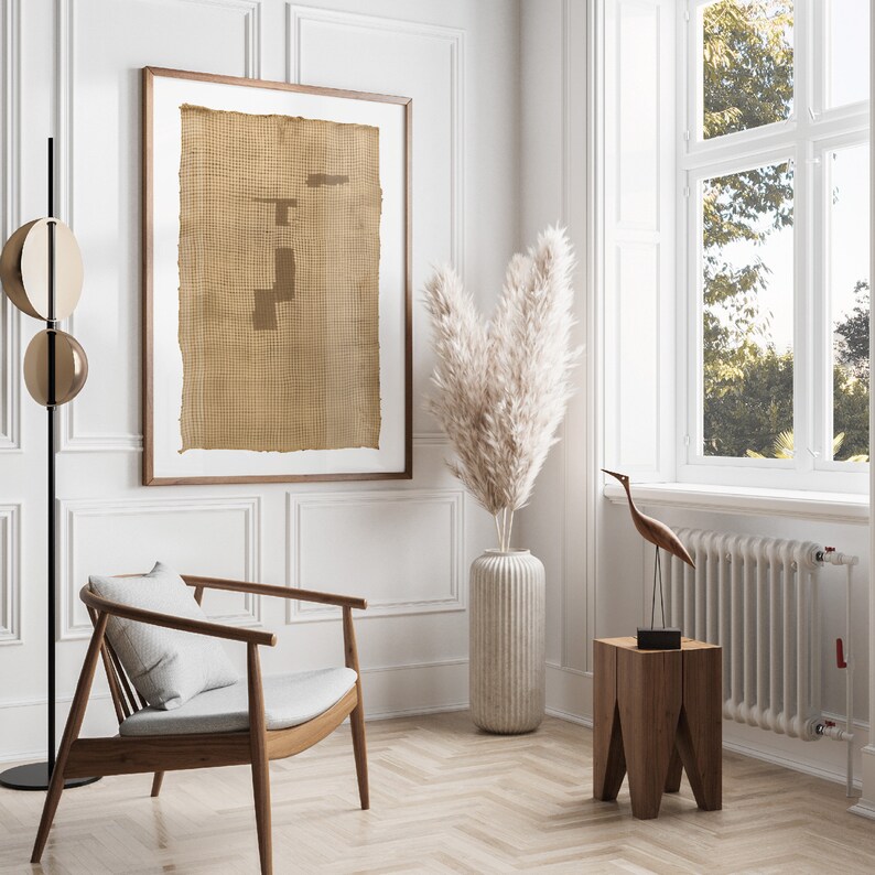 K&ouml;nnte beinhalten: Ein hellbraunes gerahmtes Kunstwerk mit einer gewebten Textur h&auml;ngt an einer wei&szlig;en Wand. Eine wei&szlig;e Vase mit getrocknetem Pampasgras steht auf dem Boden neben einem Holzhocker mit einer Holzvogelskulptur darauf.