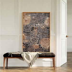 K&ouml;nnte beinhalten: Ein gerahmter abstrakter Kunstdruck mit einem Muster aus schwarzen, braunen und wei&szlig;en Punkten und Linien. Der Druck h&auml;ngt an einer wei&szlig;en Wand &uuml;ber einer Holzbank.