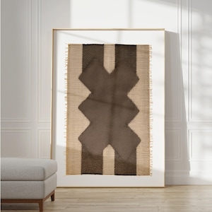 Op de afbeelding: Een ingelijst wandkleed met een geweven ontwerp in tinten bruin en beige. Het ontwerp heeft een geometrisch patroon met een centrale X-vorm.