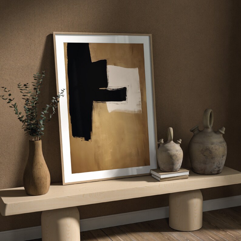 May include: A framed abstract art print with black and white shapes on a gold background. The print is displayed on a light wood shelf with two decorative ceramic jugs and a stack of books.