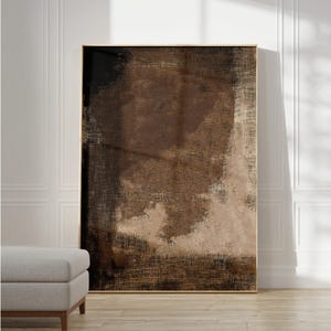 Op de afbeelding: Abstract schilderij in bruin, zwart en beige kleuren. Het schilderij heeft een textuur, alsof het op canvas is geschilderd. Het schilderij is ingelijst in een dun, gouden lijst.