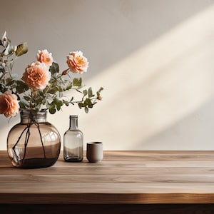 May include: A bouquet of peach-colored roses in a clear glass vase with a brown tint. The vase is sitting on a wooden table with a clear glass bottle and a small ceramic cup.