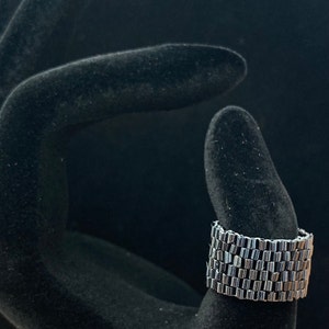 May include: A silver beaded bracelet with a stacked design. The bracelet is shown on a black velvet hand model.