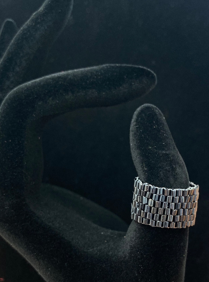 May include: A silver beaded bracelet with a stacked design. The bracelet is shown on a black velvet hand model.