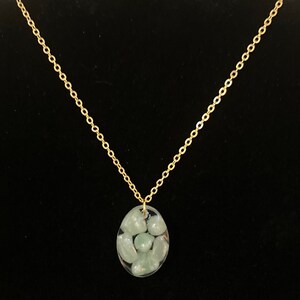 May include: A gold chain necklace with a clear pendant containing small green stones.