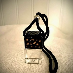 May include: A black and clear glass car air freshener with a black string hanging from it. The air freshener has a geometric pattern on the top.